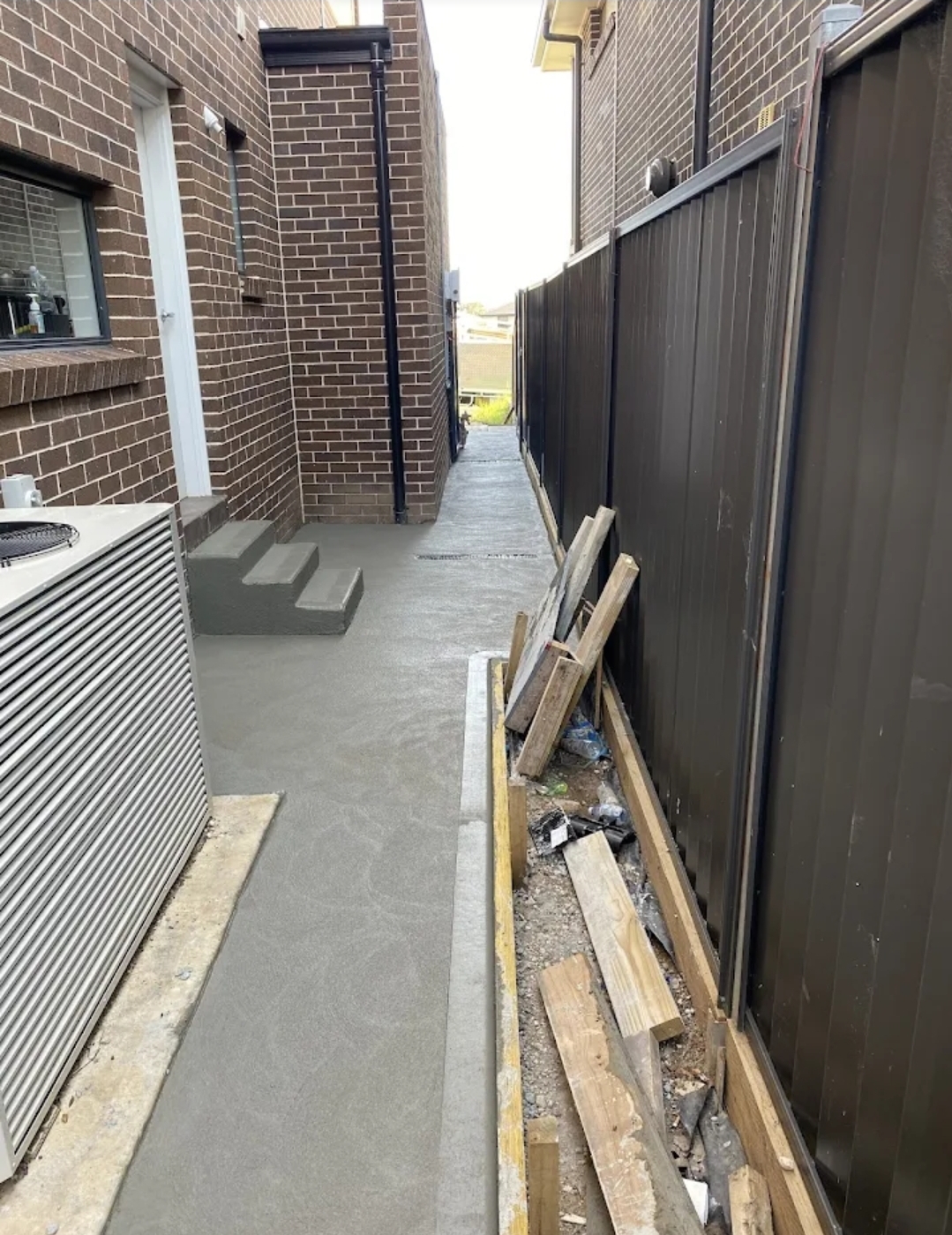 Newly poured side path running between two brick homes, with formed concrete steps to a back door