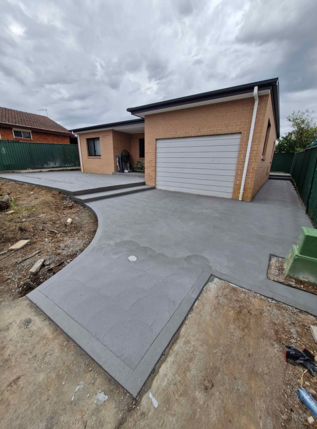 Front driveway and garage apron finished in grey concrete with a decorative bordered panel